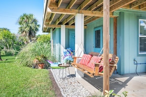 A covered porch with a wooden swing, a small table, and a potted plant. - 4BR Beach Cottage Pool Walk to Beach (St. Augustine)