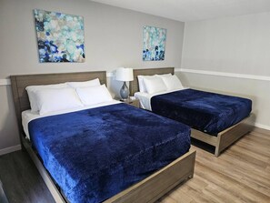 A hotel room with two beds, each with a blue bedspread and white pillows. There are two wall-mounted paintings above the beds.