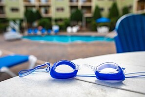 A pair of blue swimming goggles on a table with a pool and hotel buildings in the background. - Pigeon Forge | Romantic Mountain Retreat | Trails + Attractions (Pigeon Forge)