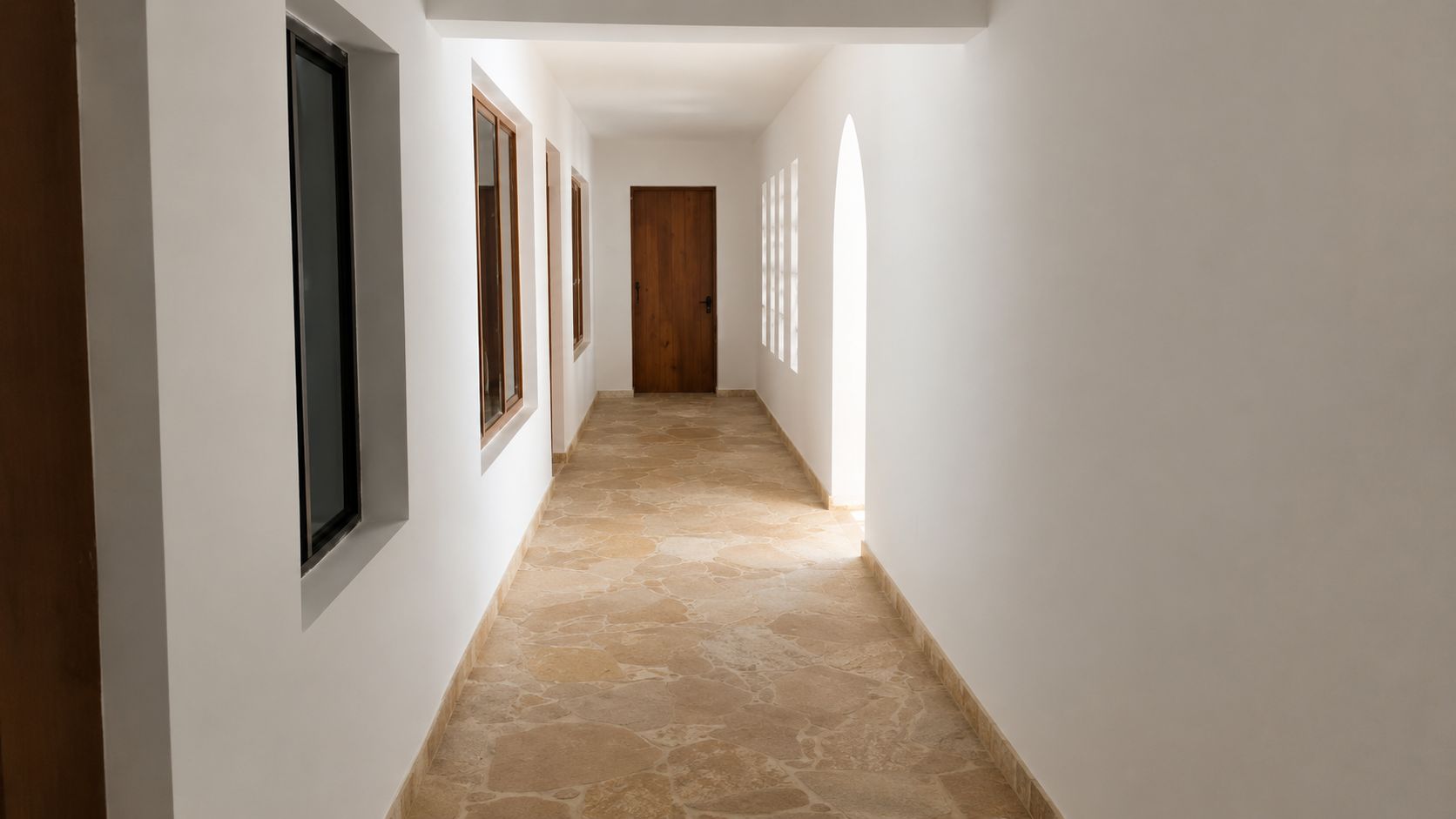 A corridor with stone flooring, white walls, and wooden doors.