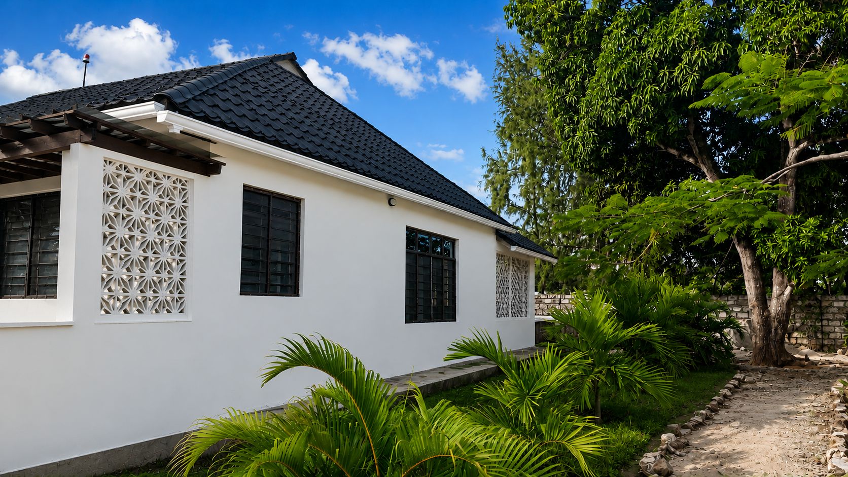 A white building with a dark roof, surrounded by lush greenery and a clear sky.