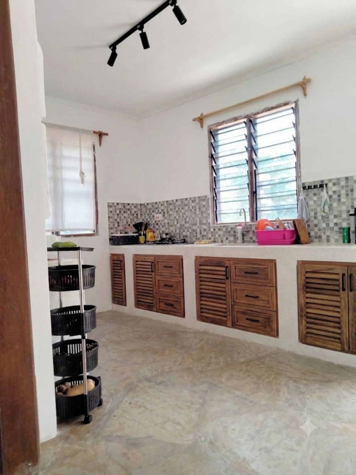 A kitchen with a tiled backsplash, wooden cabinets, and a window with blinds.
