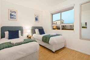 A hotel room with two beds, a nightstand, a lamp, and a window with a view of buildings. - Sea Spray A109 (Cape Town)