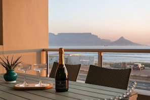 A balcony with a table set for two, a bottle of champagne, and two glasses. - Sea Spray A109 (Cape Town)