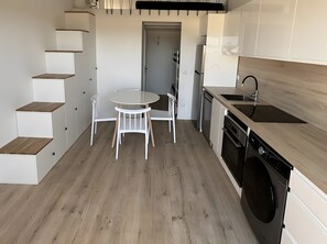 A compact kitchen with a round table, white chairs, a built-in dishwasher, and a washing machine. - Apartment 'Studio Plage et Village' with Sea View, Shared Pool and Air Conditioning (Le Barcarès)
