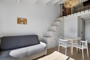 A modern living space with a grey sofa, white chairs, a small table, and a wall-mounted shelf unit. - Apartment 'Studio Plage et Village' with Sea View, Shared Pool and Air Conditioning (Le Barcarès)