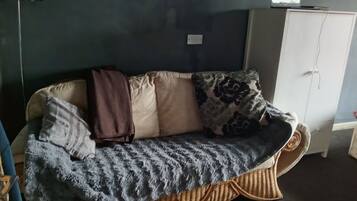 A room with a sofa against a dark wall, a cabinet, and a small television on top.