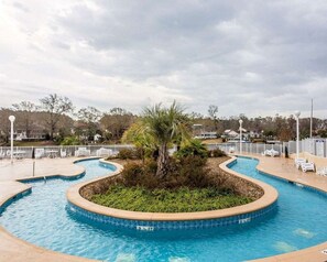 Une piscine bordée d’un palmier, entourée d’une clôture blanche et de chaises longues.