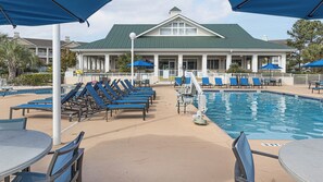 A poolside area with lounge chairs and umbrellas, a pool, and a building with a green roof. - Myrtle Beach | Poolside Leisure Days | Lazy River + Hot Tub (Myrtle Beach)