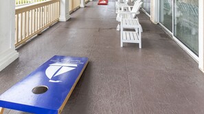 A covered outdoor area with a shuffleboard table, white chairs, and a glass wall. - Myrtle Beach | Poolside Leisure Days | Lazy River + Hot Tub (Myrtle Beach)