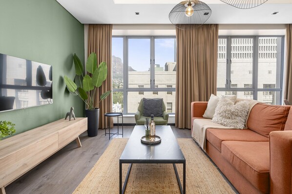 Ein modernes Wohnzimmer mit einer Couch, einem Couchtisch und einem großen Fenster mit Vorhängen.
