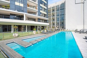Un edificio moderno con piscina, mobiliario exterior y césped bien cuidado.