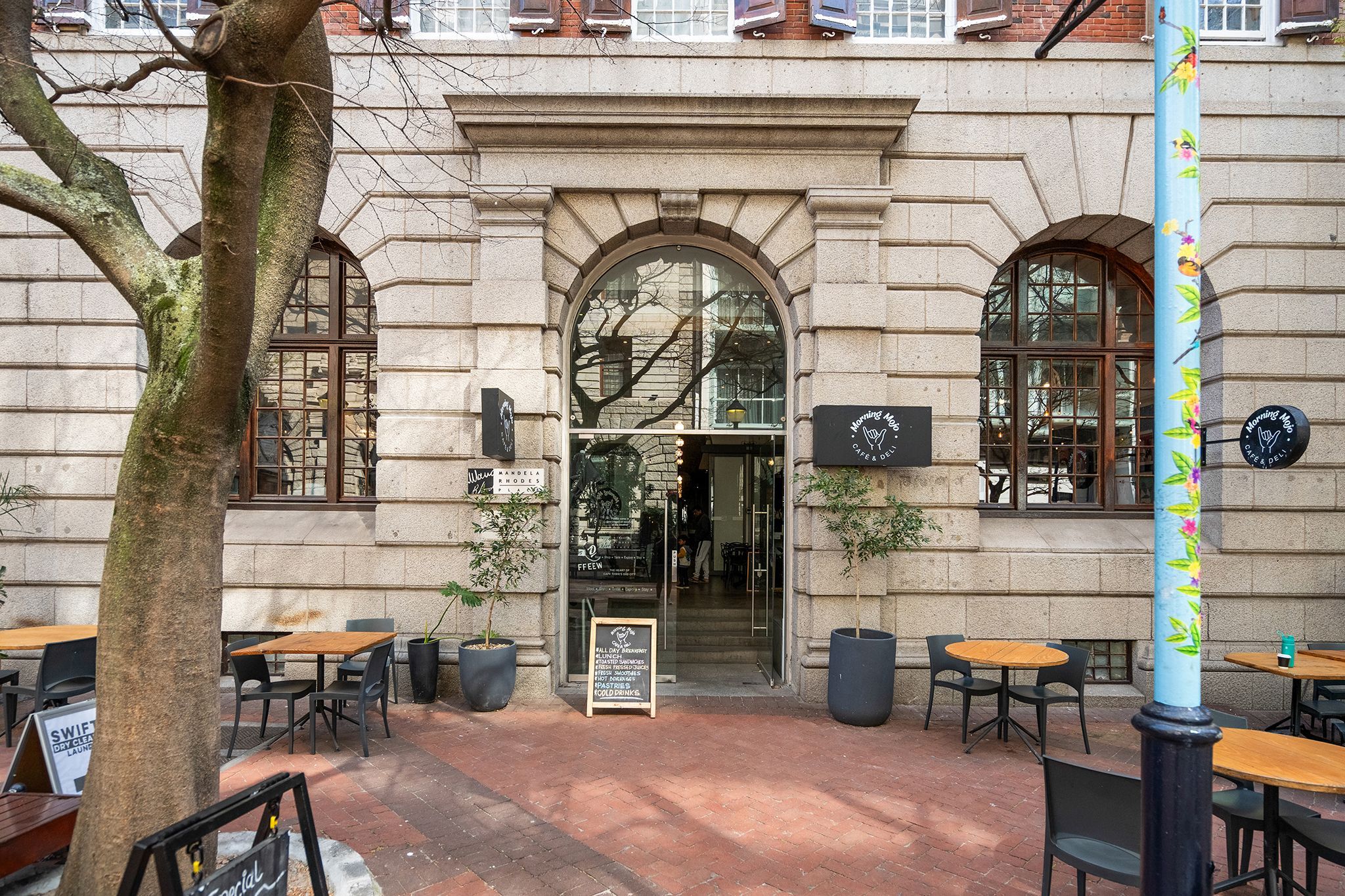 A cafe with outdoor seating, a stone facade, and a sign for 'Morning Mojo Cafe & Deli'.
