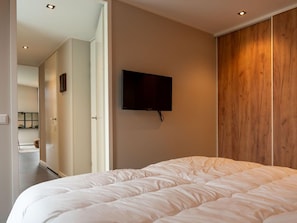 Ein Schlafzimmer mit einem großen Bett, einem an der Wand montierten Fernseher und einem Holzschrank.