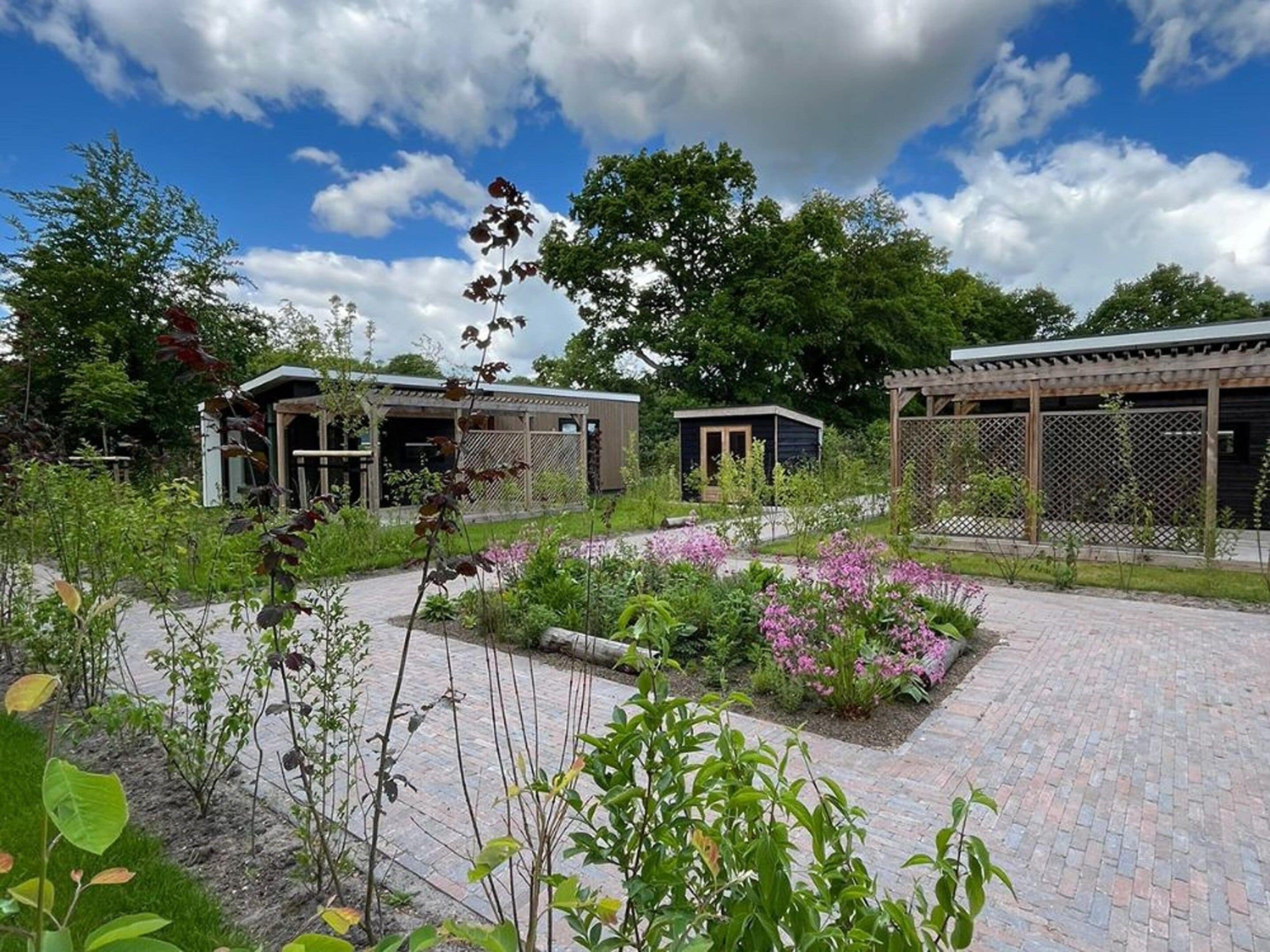A garden area with pathways, a wooden pergola, and two small buildings with open sides.