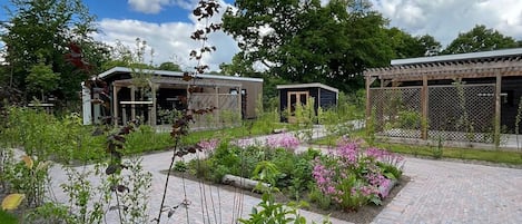 A garden area with pathways, a wooden pergola, and two small buildings with open sides.