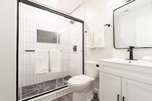 Et stilfuldt badeværelse med en brusekabine i glas, hvide fliser, et toilet i hvidt og en vask med spejl.