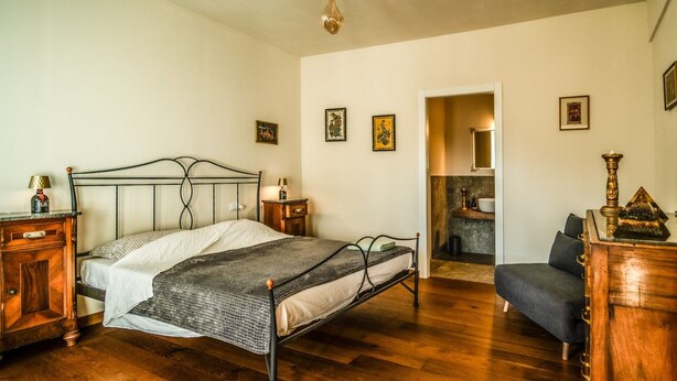 A bedroom with a bed, bedside tables, a dresser, a chair, and a bathroom visible through an open door. - defaultName (Monte Castello di Vibio)