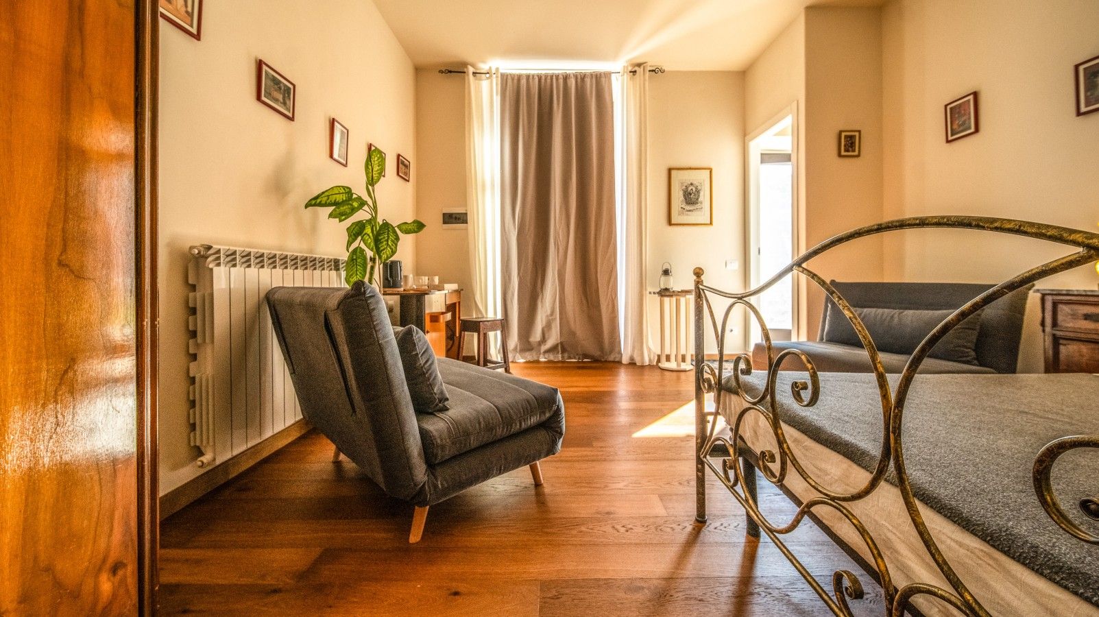 A room with a bed, a chair, a radiator, a plant, and a window with curtains.