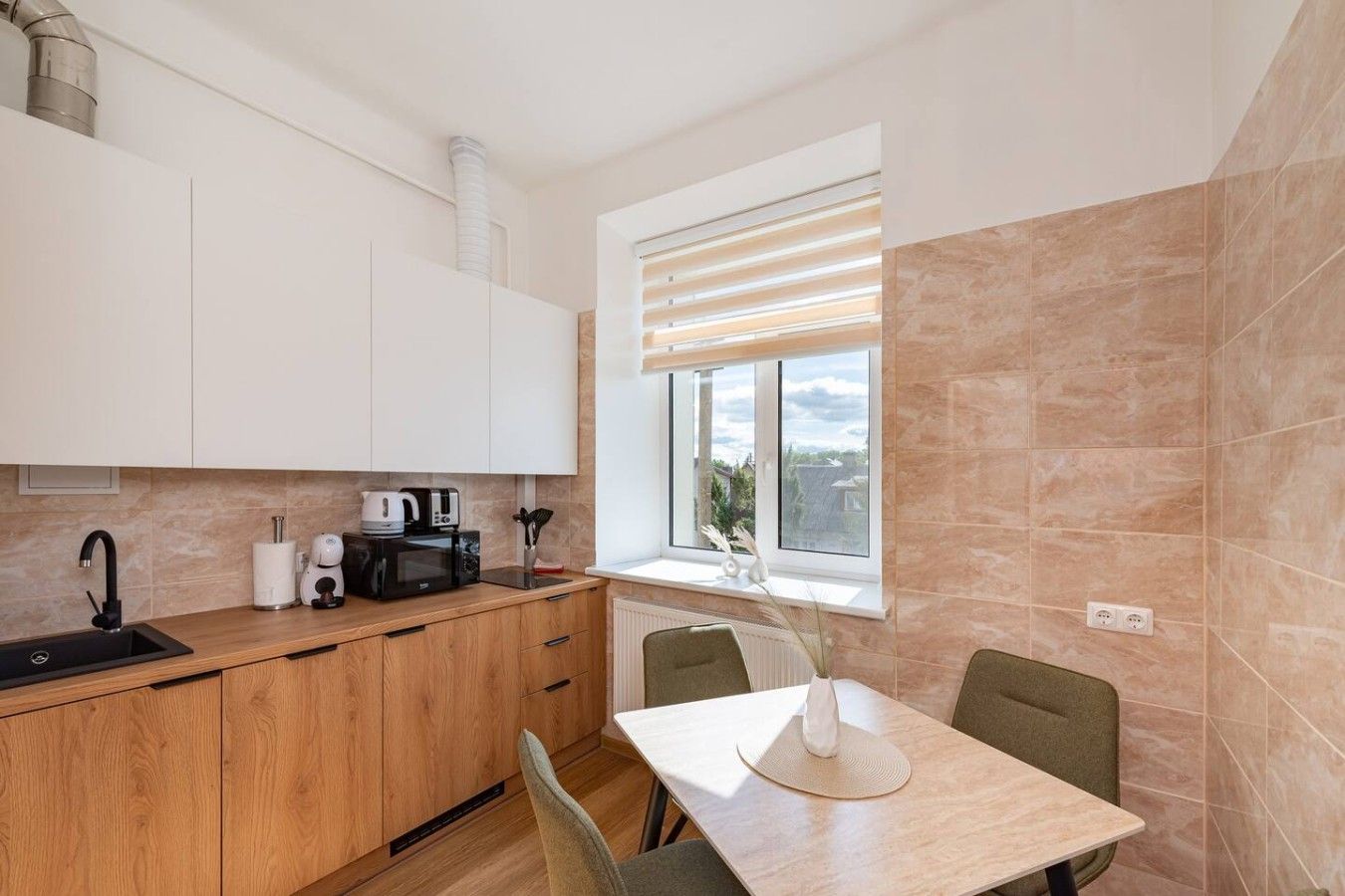 Eine kompakte Küche mit Spüle, Herd und Mikrowelle, Holzschränken, einem Fenster mit Jalousien und einem Essbereich mit Tisch und Stühlen.