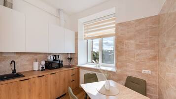 Eine kompakte Küche mit Spüle, Herd und Mikrowelle, Holzschränken, einem Fenster mit Jalousien und einem Essbereich mit Tisch und Stühlen.