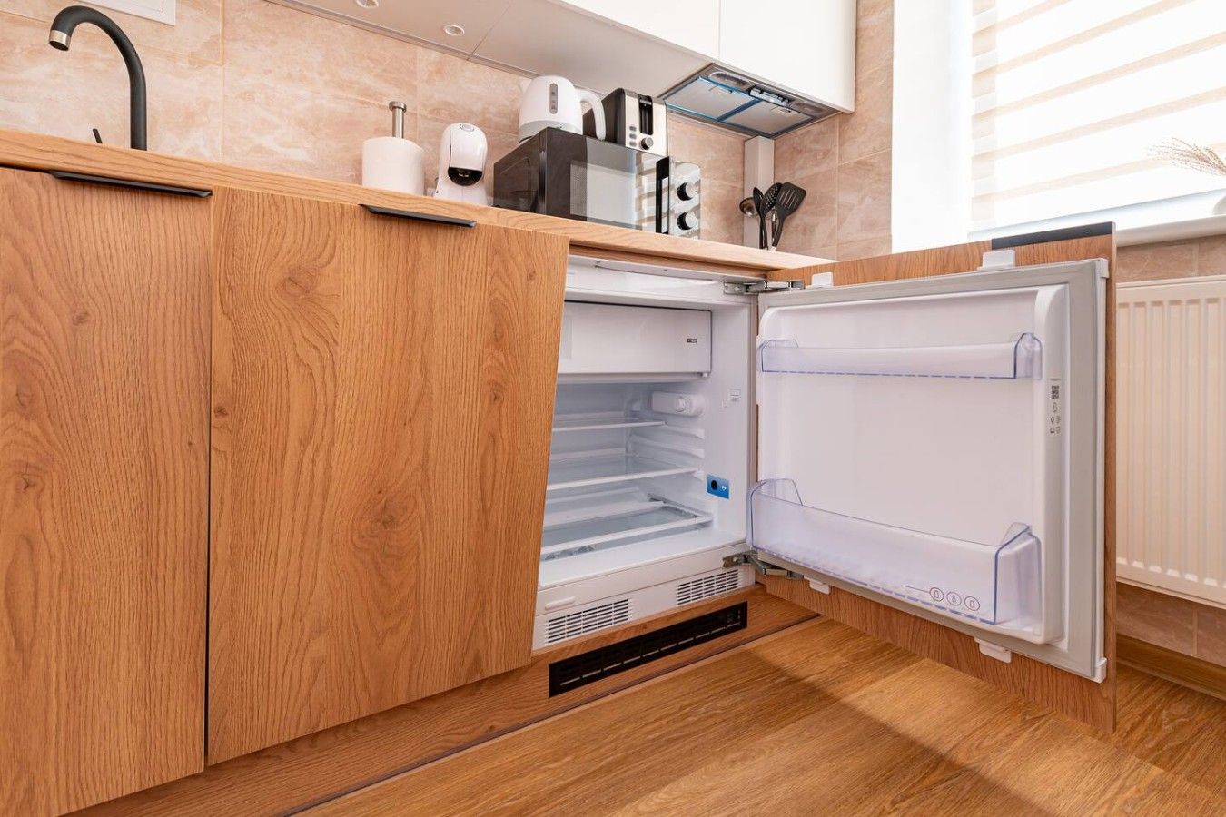 A kitchen with wooden cabinets, a built-in microwave, and a refrigerator.
