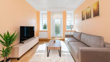 Ein modernes Wohnzimmer mit Fernseher, einem beigen Sofa, einem Couchtisch und einem Blumentopf.