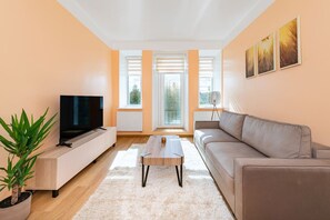 Una sala de estar moderna con un televisor de pantalla plana, un sofá color beige, una mesa de centro y una planta en maceta.