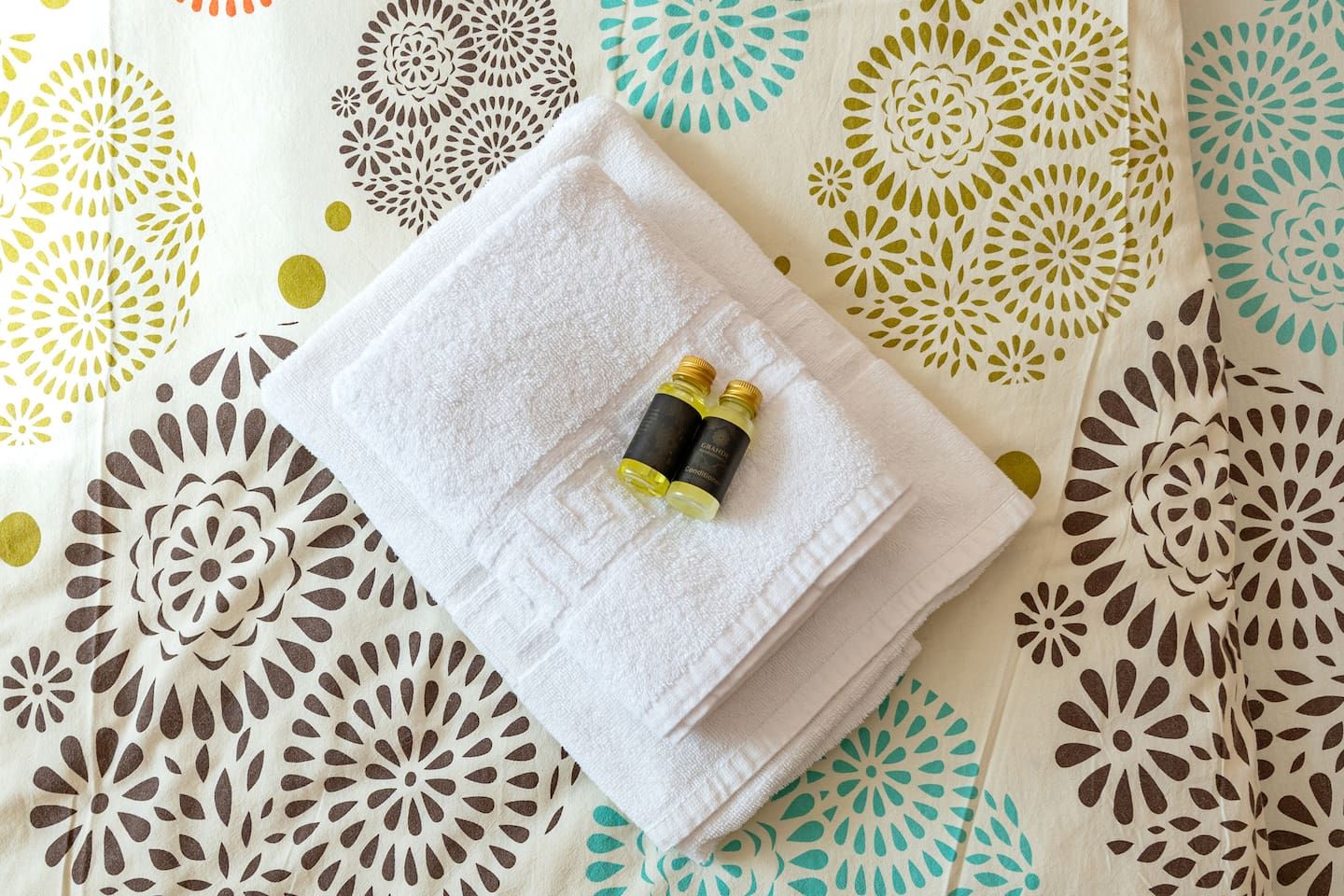 A neatly folded white towel on a patterned bedspread.