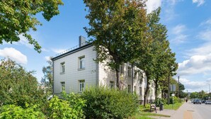 A two-story building with a light-colored facade, surrounded by greenery and a clear sky. - Dariaus and Girėno Ap. by Polo Apartments (Kaunas)