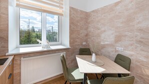A dining area with a table, chairs, a window with blinds, a radiator, and a view of the outside. - Dariaus and Girėno Ap. by Polo Apartments (Kaunas)