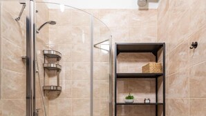 A compact bathroom with a glass-enclosed shower, a built-in washing machine, and a storage shelf with baskets. - Dariaus and Girėno Ap. by Polo Apartments (Kaunas)
