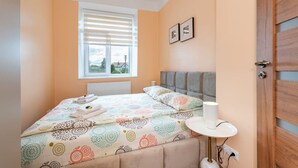 A bedroom with a bed, a bedside table, a window with blinds, and a door. - Dariaus and Girėno Ap. by Polo Apartments (Kaunas)