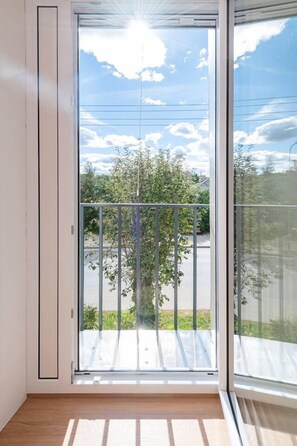 Een kamer met een grote schuifpui die uitkomt op een balkon met een metalen hekwerk.