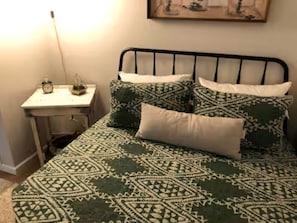 Una cama con ropa de cama estampada, una mesita de noche con lámpara y un cuadro colgado en la pared.