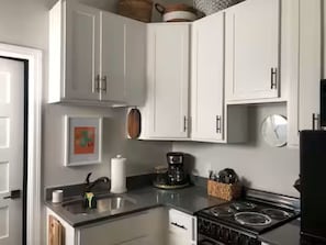 Una cocina con armarios blancos, estufa, cafetera y lavaplatos.
