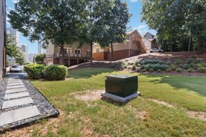 A residential area with a paved walkway, a green lawn, and a large green utility box. - Modern 3BR Home Near Midtown & Atlantic Station (Atlanta)