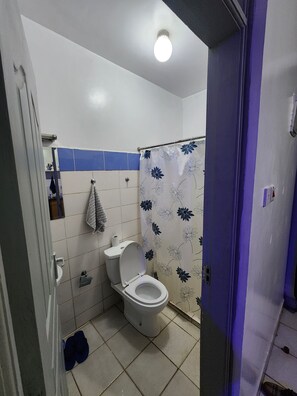 A bathroom with a toilet, a shower curtain with a floral pattern, and a towel hanging on the wall. - 
Cozy Modern Studio on Ngong Road (Nairobi)