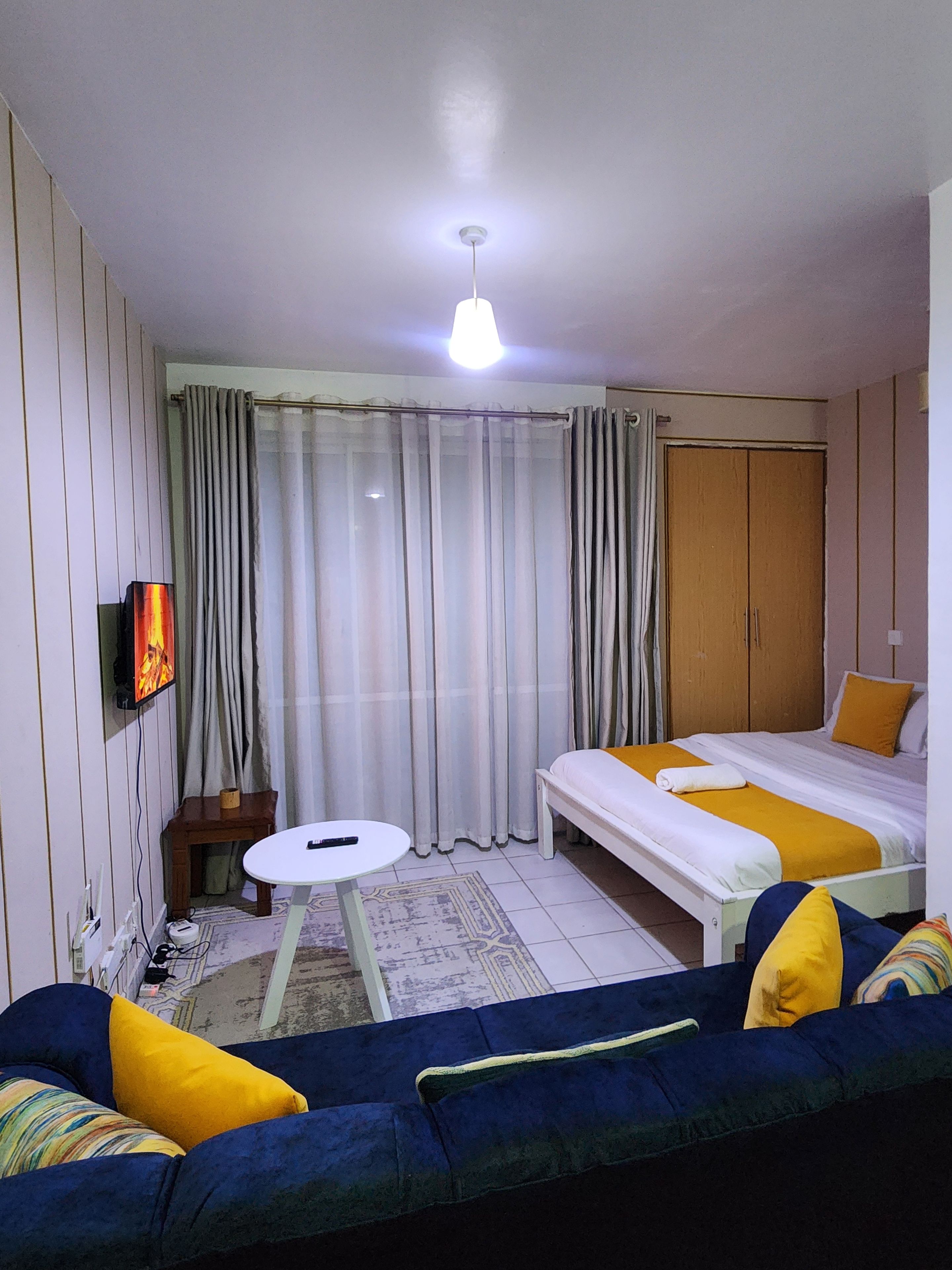 A hotel room with a bed, a sofa, a small table, and a television.