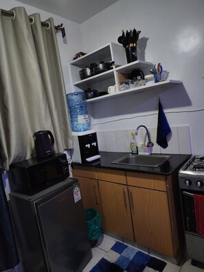 A compact kitchen with a refrigerator, microwave, stove, sink, and a water dispenser. - 
Cozy Modern Studio on Ngong Road (Nairobi)