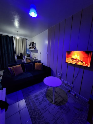 A living room with a sofa, a coffee table, a flat-screen TV, and a kitchen area in the background. - 
Cozy Modern Studio on Ngong Road (Nairobi)