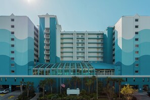 A multi-story hotel with a modern design, featuring a central glass facade and a symmetrical layout. - North Myrtle Beach | Beach Escape | Pool & Ocean Access | 1BR Villa (North Myrtle Beach)