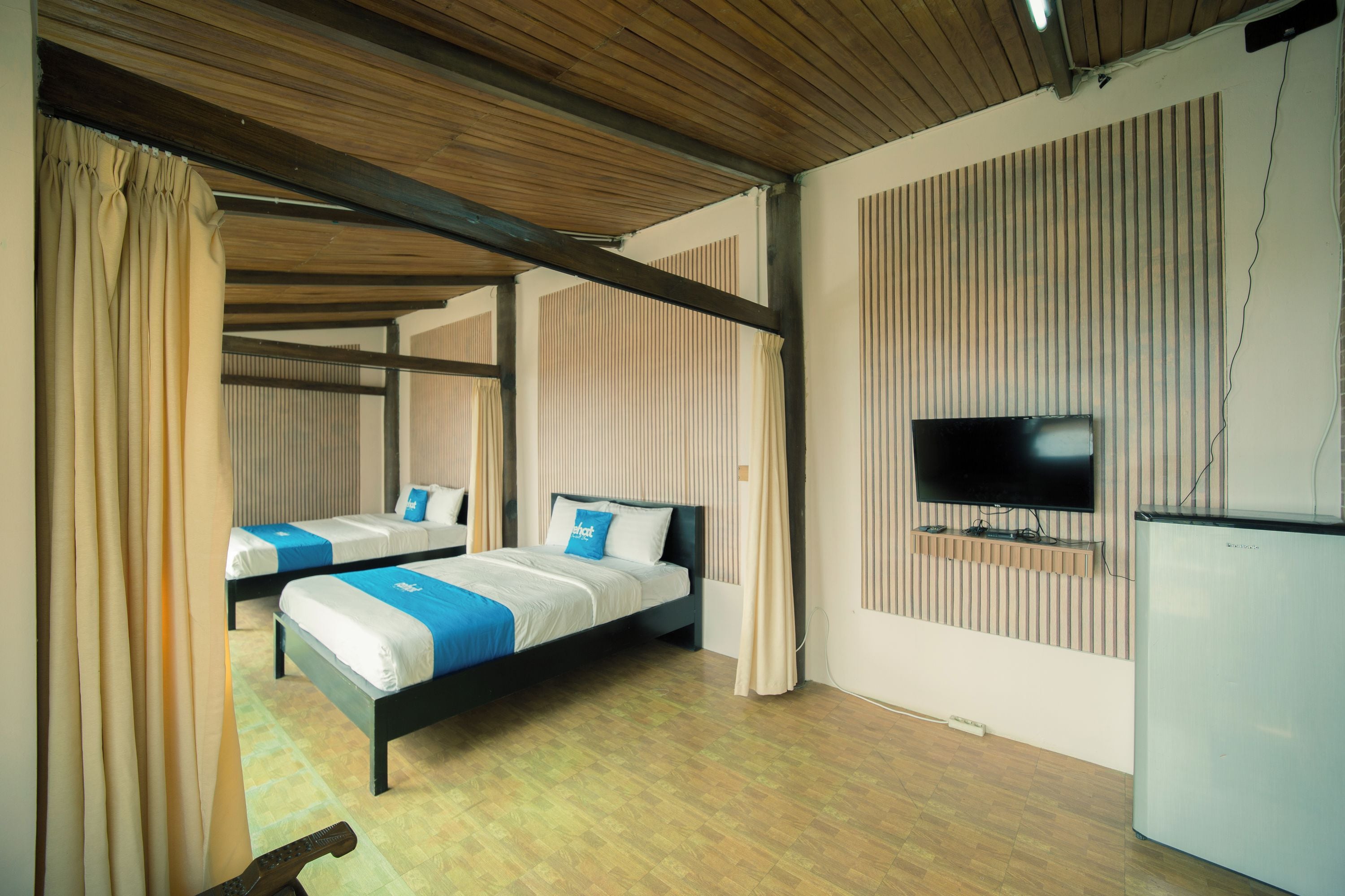 Ein Hotelzimmer mit zwei Betten, einem Fernseher und einem Kühlschrank.