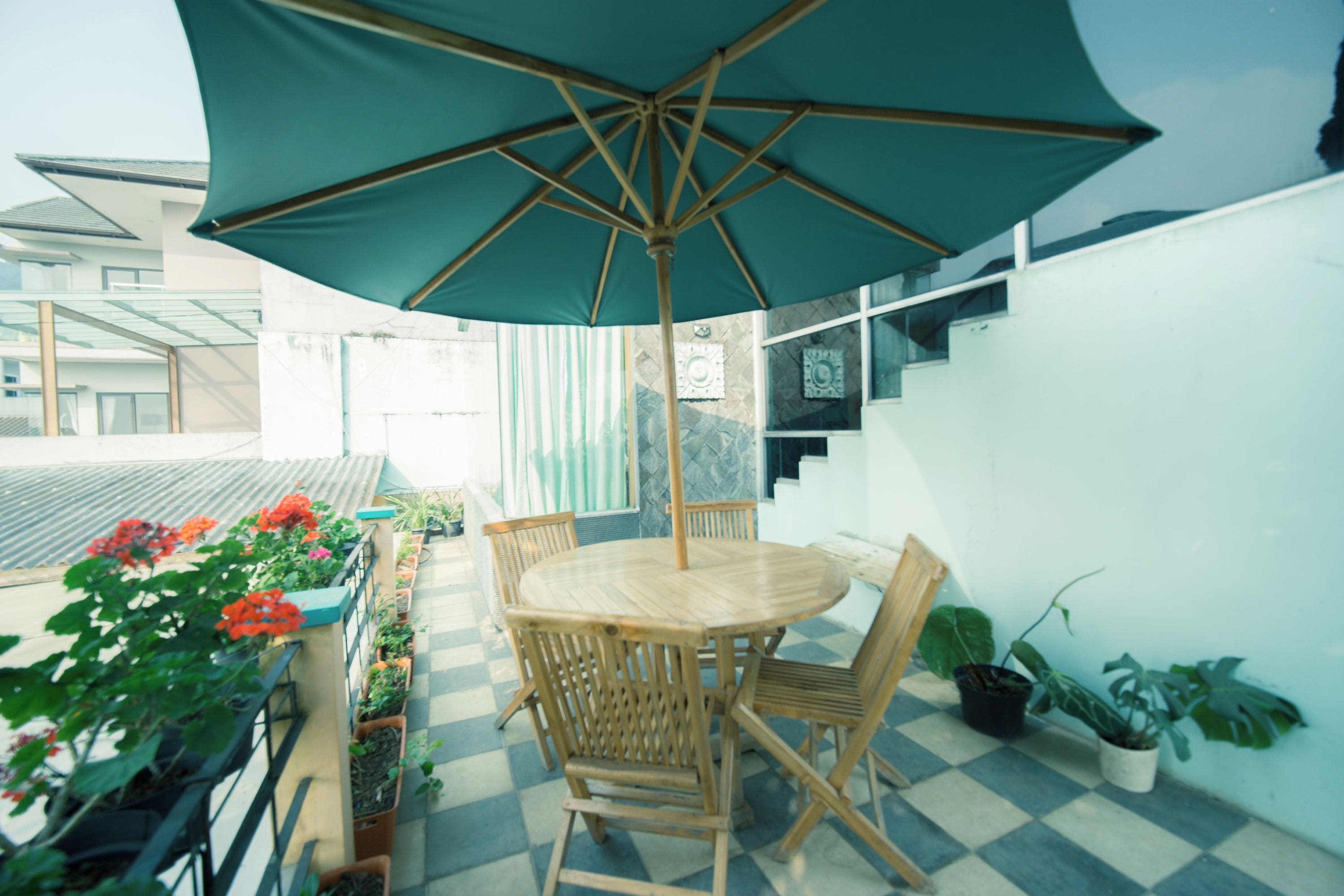 An outdoor patio area with a wooden table and chairs, a large umbrella, and potted plants.