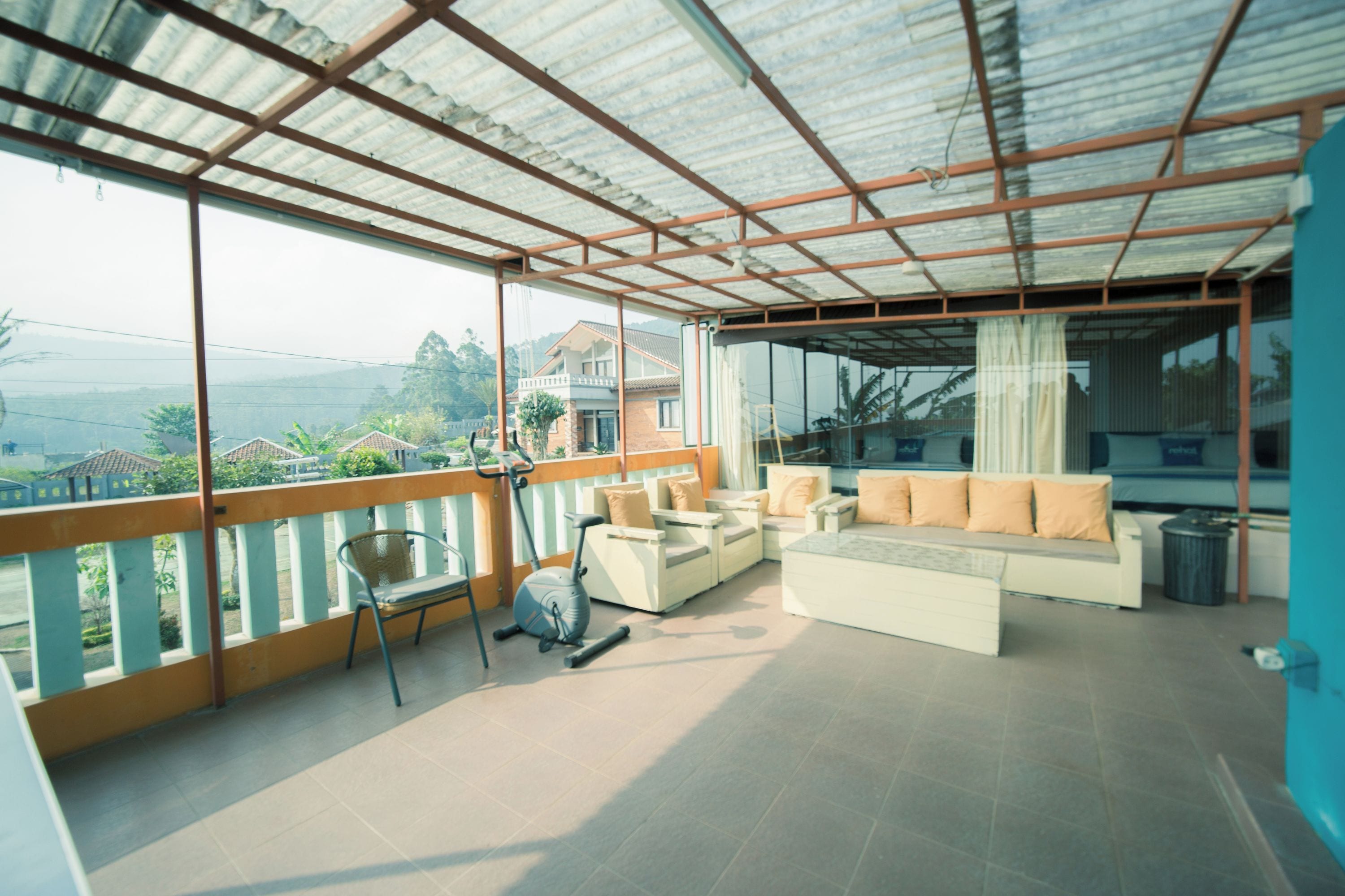 A spacious balcony with a view of the surrounding landscape, furnished with a sofa, chairs, and an exercise bike.