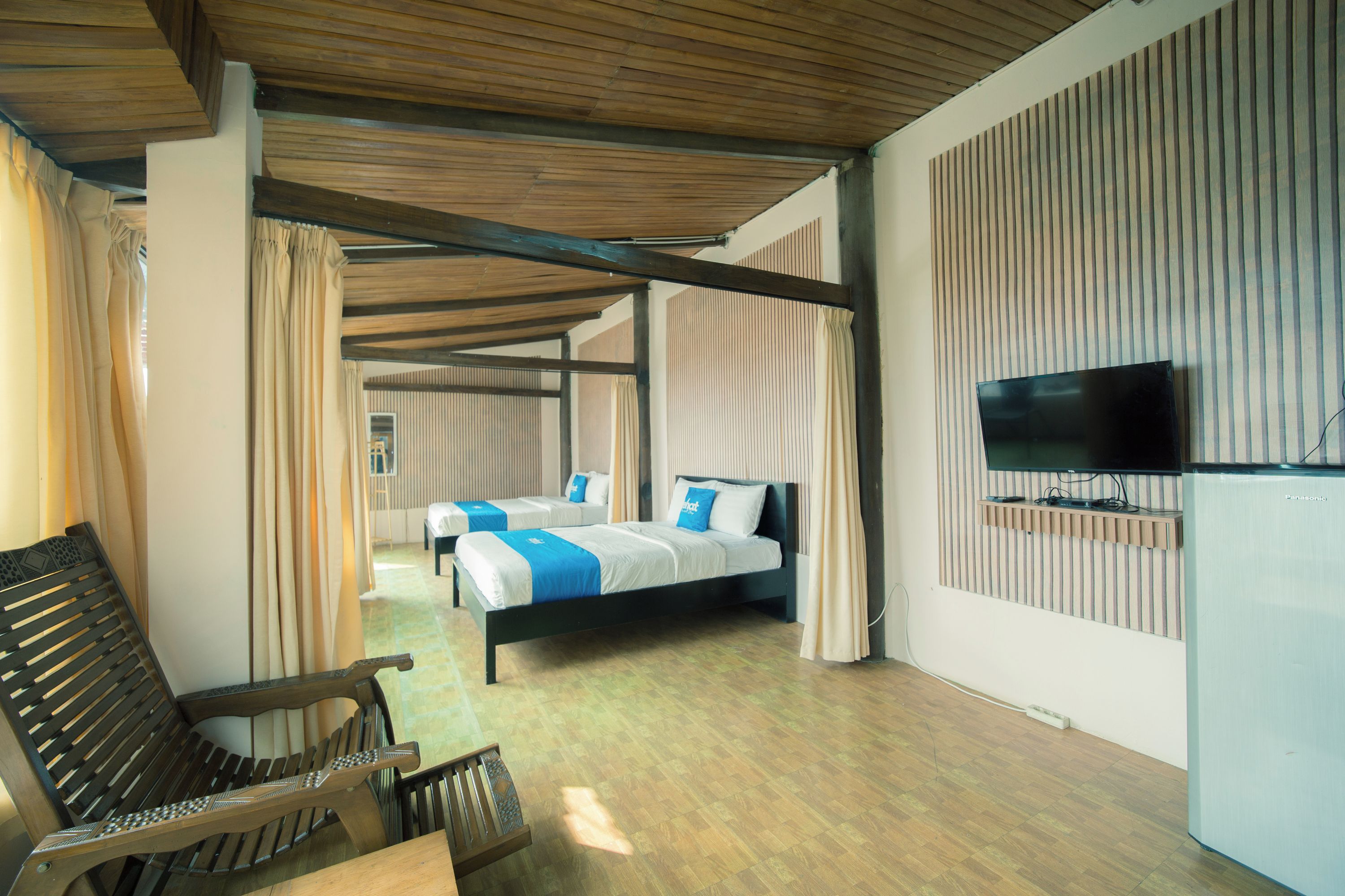 Ein Hotelzimmer mit Holzboden, einem Bett mit blauer Bettwäsche, einer Bank und einem an der Wand befestigten Fernseher.