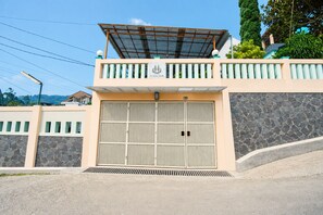 A gated entrance with a metal gate, a stone wall, and a covered balcony area. - Rehat at Villa Cemara Kembar (Kabupaten Bandung)