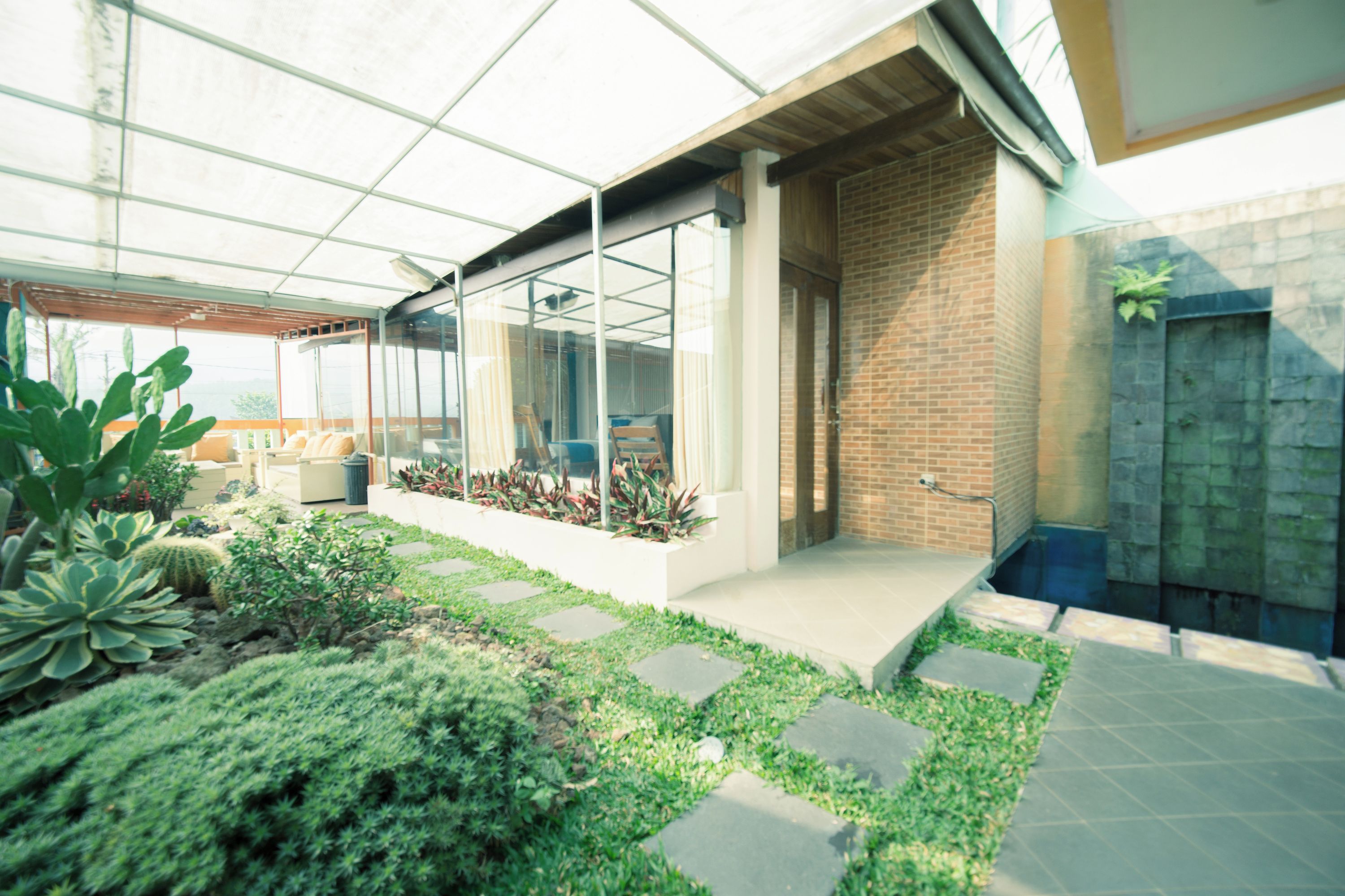 Eine moderne Außenpatio mit Glasveranda, Backsteinmauer und verschiedenen Pflanzen.