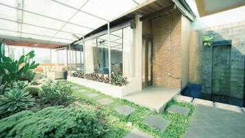 Eine moderne Außenpatio mit Glasveranda, Backsteinmauer und verschiedenen Pflanzen.