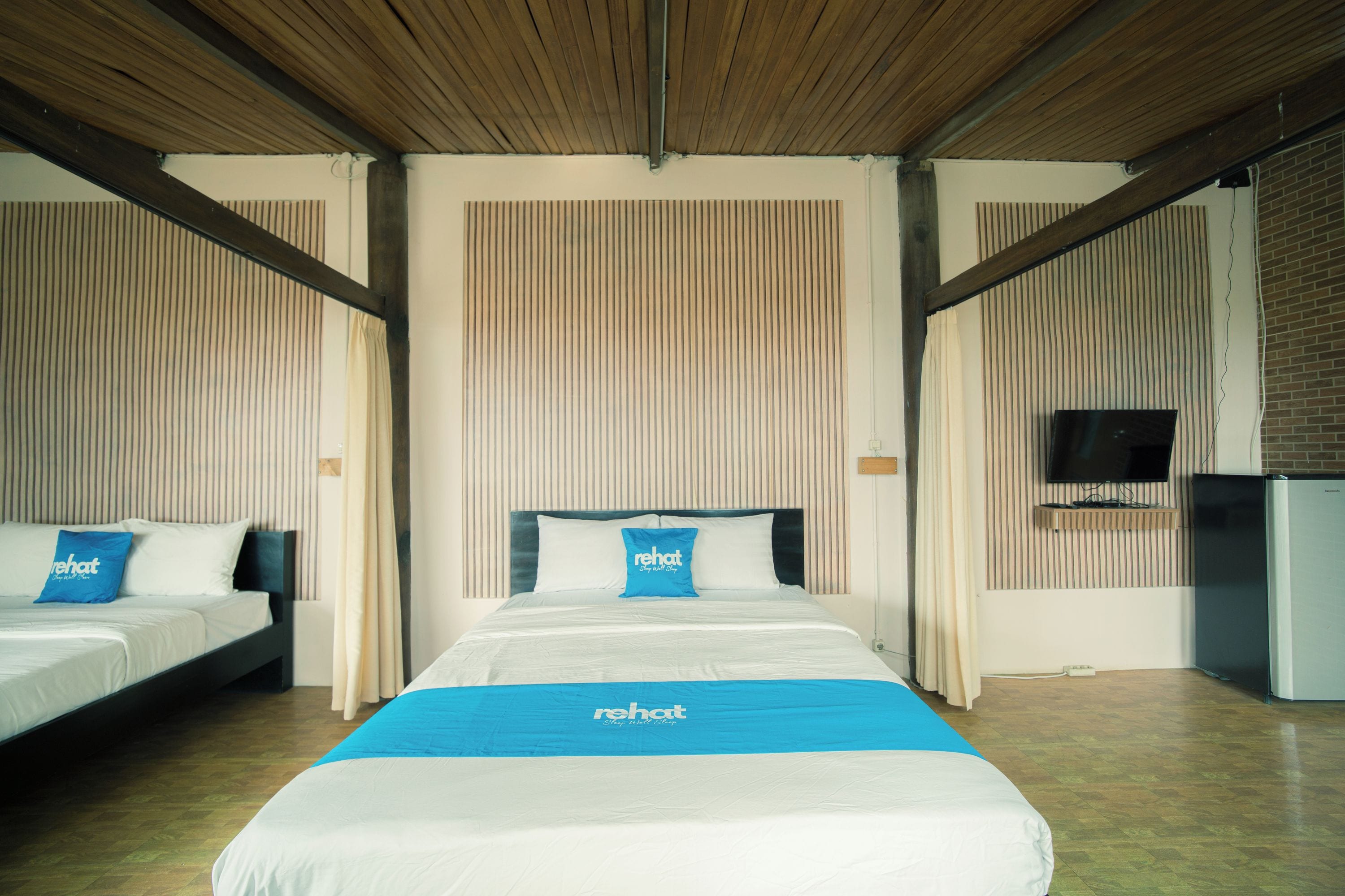 Una habitación de hotel con una cama grande, dos camas más pequeñas, un televisor y una pared de ladrillo.
